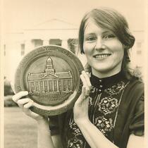 Judy Sutcliffe holding a commemorative plate in front of the Old Capitol, The University of Iowa, 1972